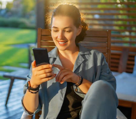Smiling woman using a smartphone while sitting outside on a chair